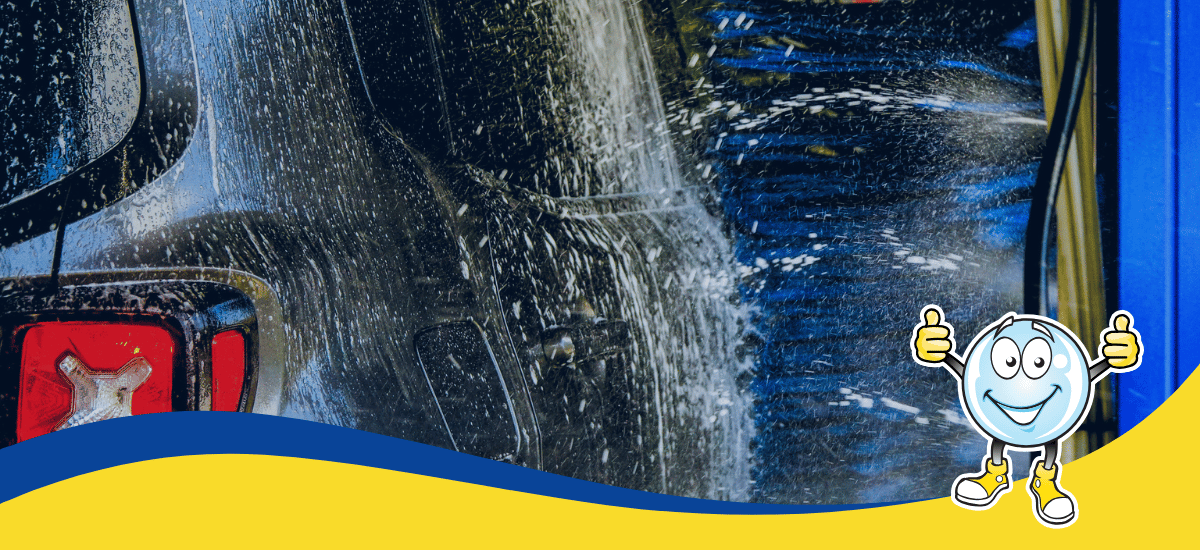 A close-up of a dark car being washed with soapy water at an automatic car wash highlights car wash water conservation. In the foreground, a cartoon water droplet character gives two thumbs up on a blue and yellow wavy border.